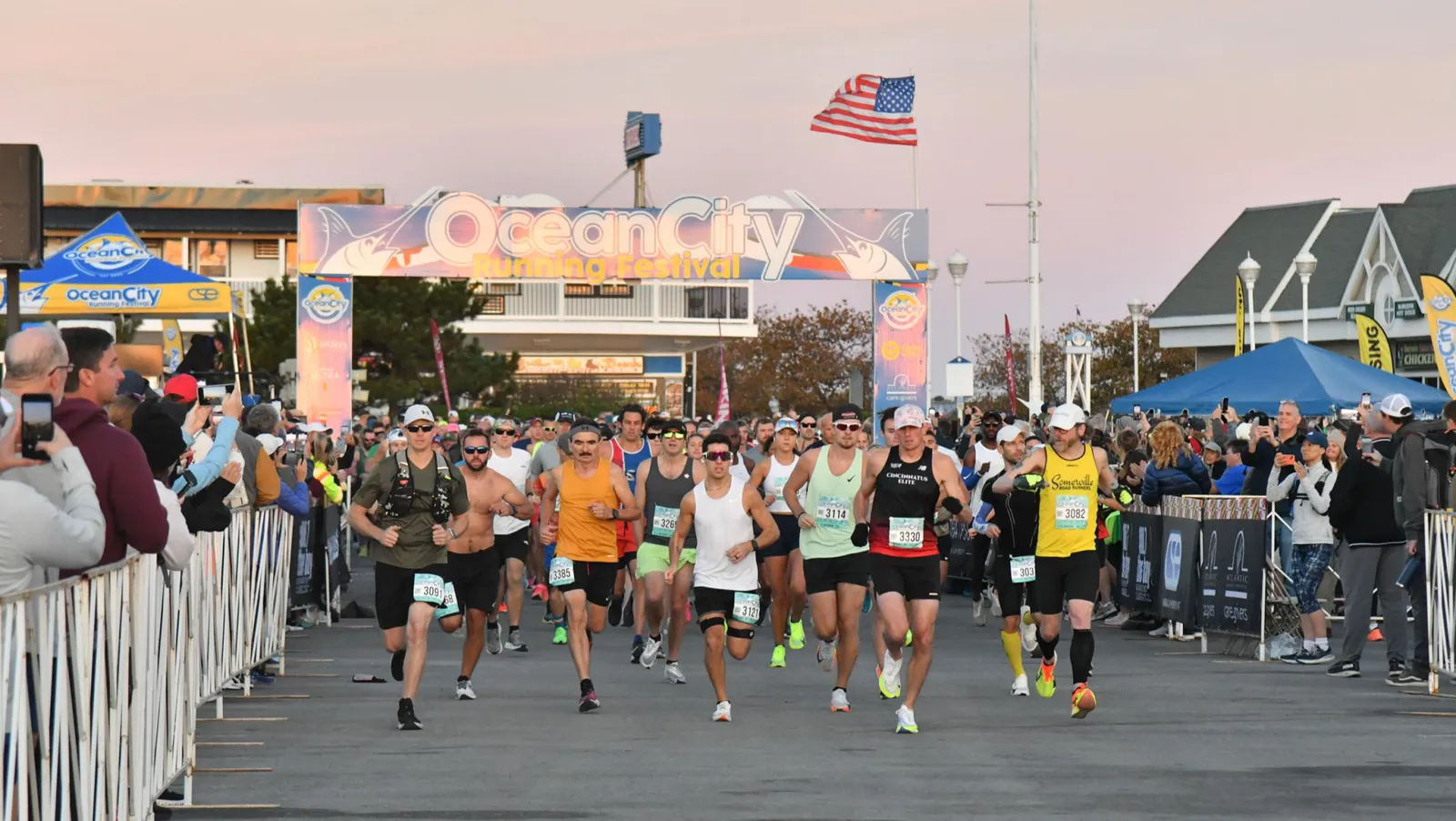 Runners starting the Ocean City Running Festival with the race archway and an American flag in the background.