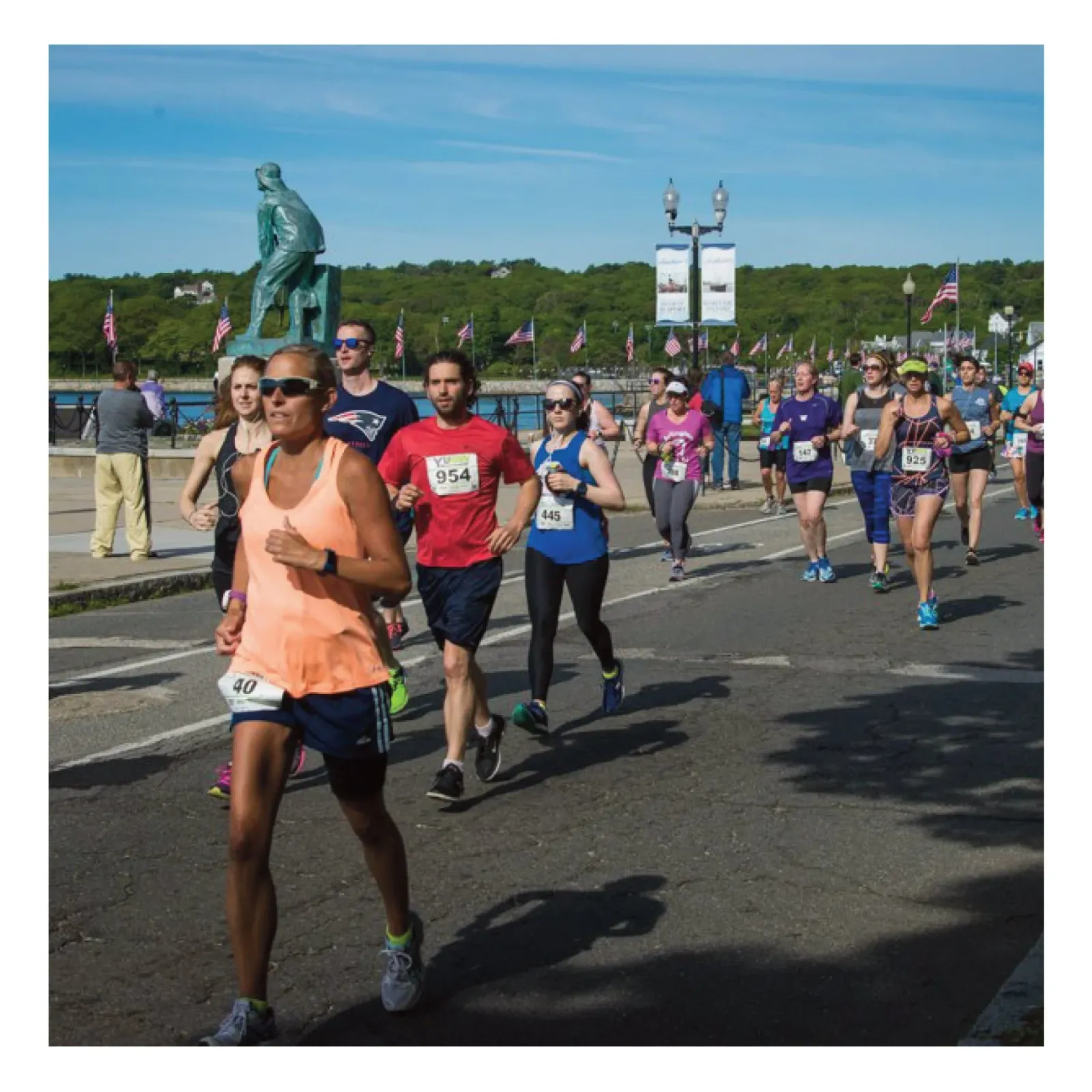 Runners participating in the Ocean View Half Marathon and 5K race, with flags and a statue visible in the background along a waterfront course.