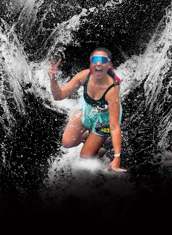 A runner wearing sunglasses and a black tank top splashes through water, holding up a peace sign and smiling.