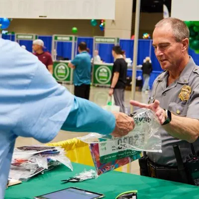 A police officer hands a race packet to a person at a registration booth.