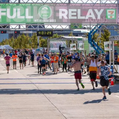 Runners celebrating as they cross the finish line at a race, with a large banner overhead and spectators in the background.