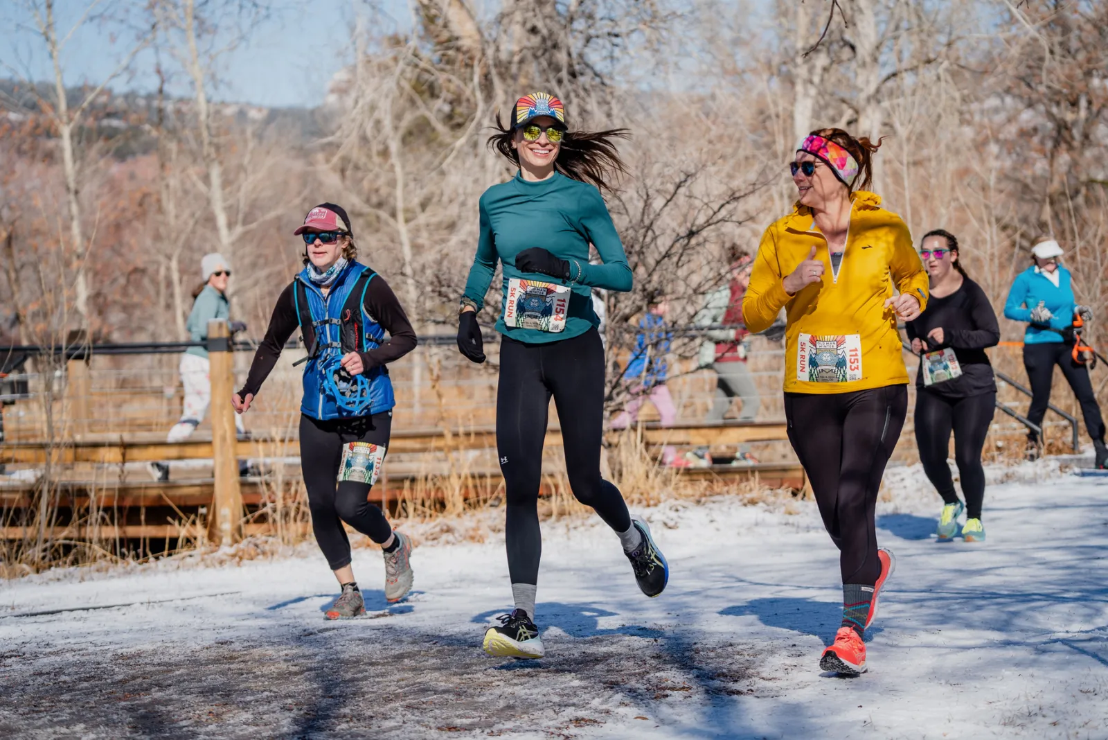 Runners on a snowy path with trees in the background.