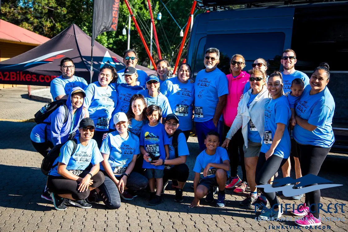 A group of runners in blue t-shirts with 'The Struggle Is Real' printed on them pose for a photo, with tents and a van in the background.
