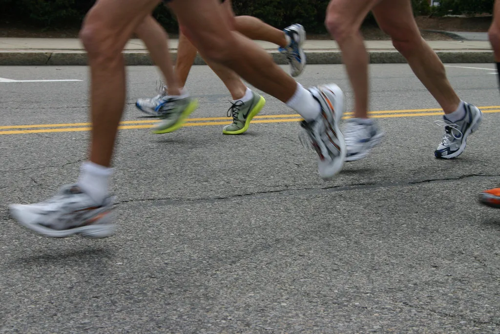 Close-up of runners' legs and feet as they race on a road, with motion blur indicating speed.