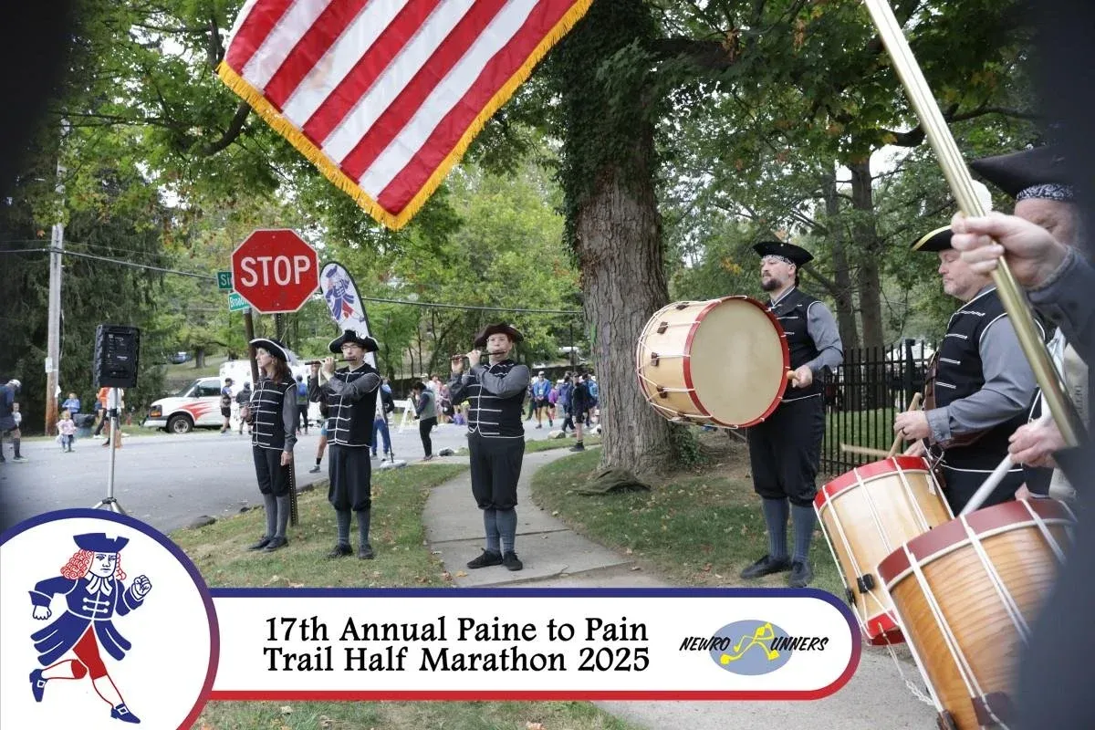 A historical reenactment group playing drums and flutes at the start of the 17th Annual Paine to Pain Trail Half Marathon 2025, with runners and spectators in the background.