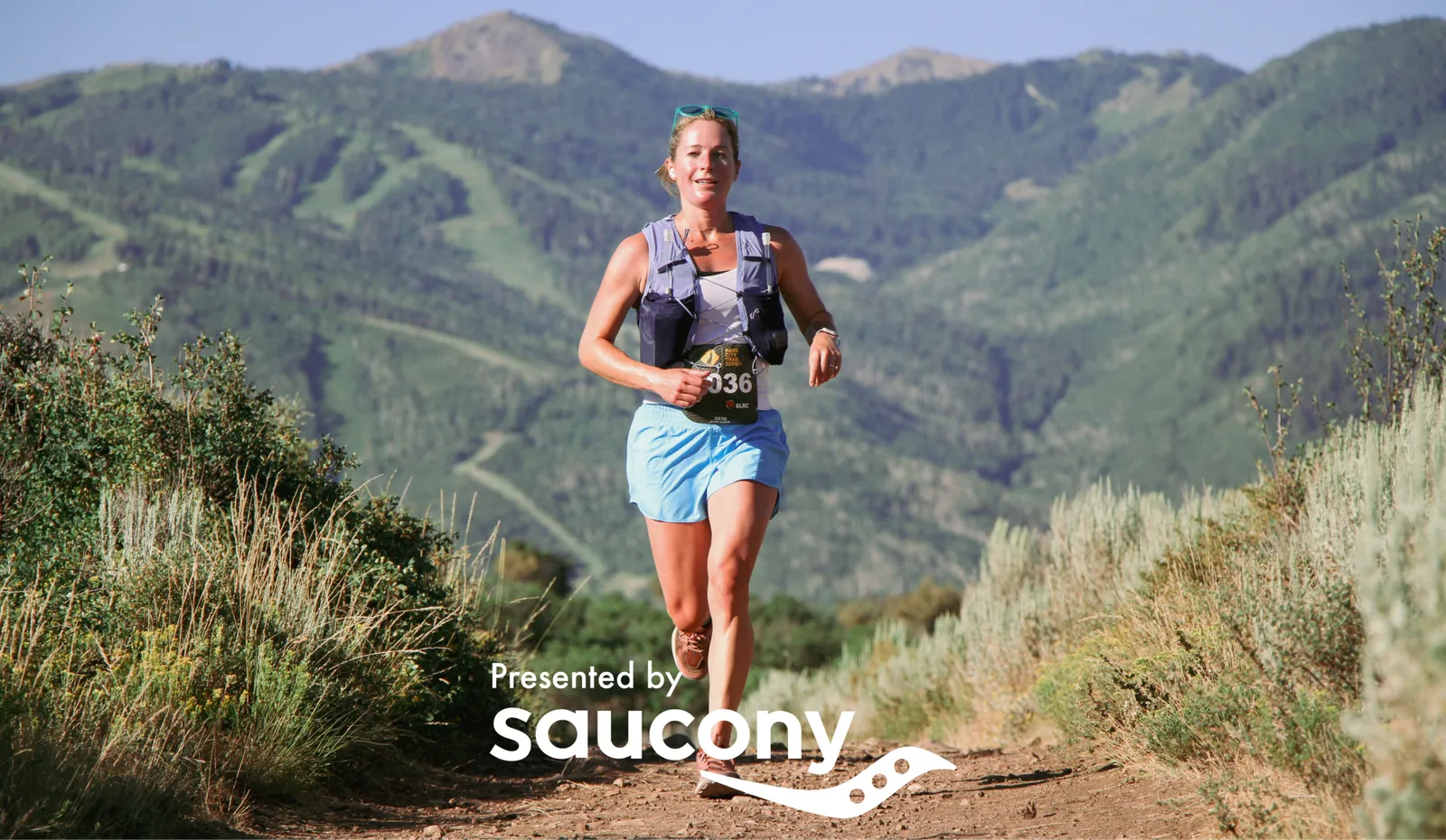 A female runner with bib number 036 runs on a dirt trail with mountains in the background.