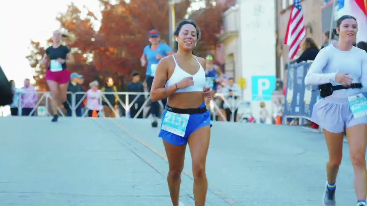 Runners participating in a race, with one runner in the foreground wearing a white sports bra and blue shorts with bib number 2131.
