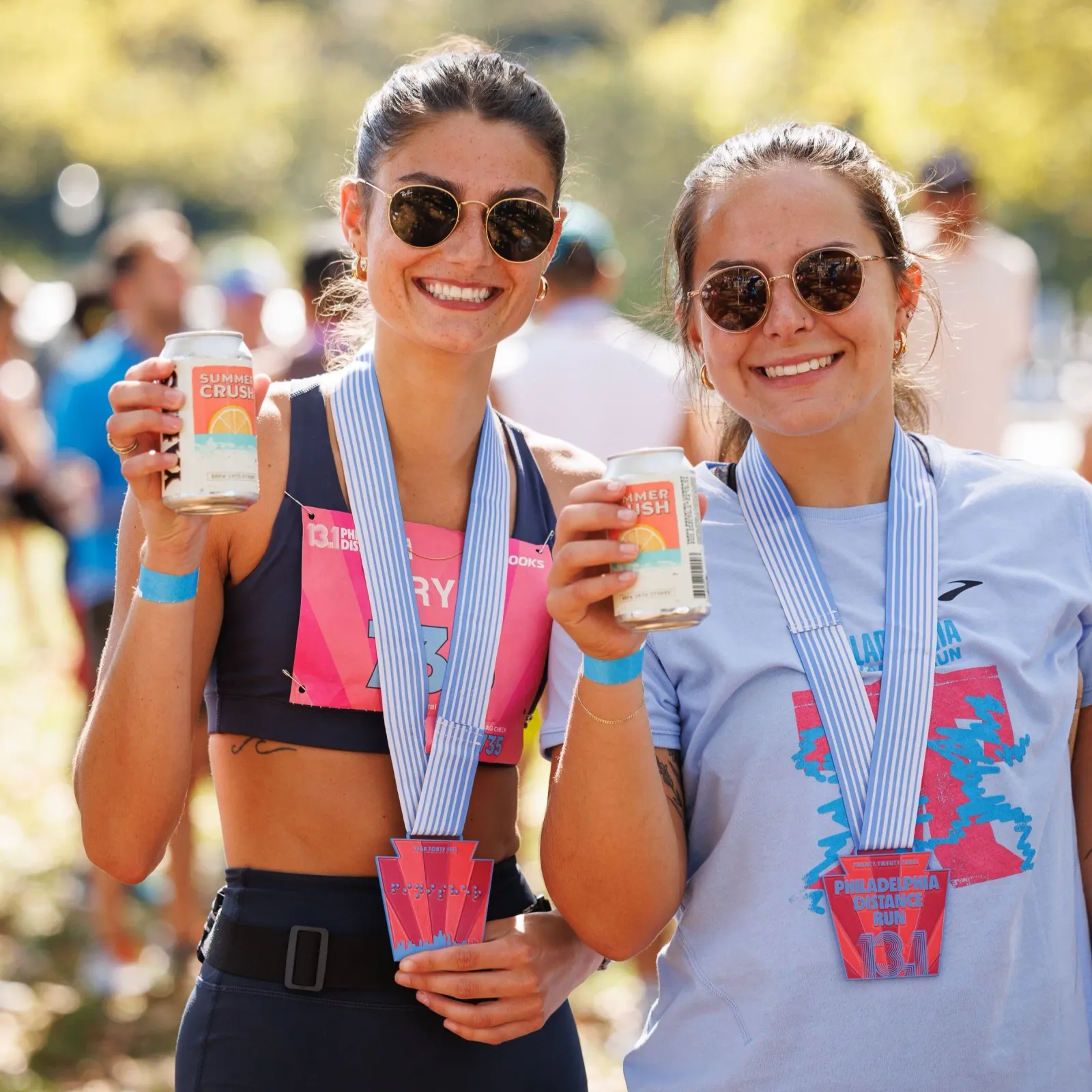 Two smiling women wearing race medals and holding cans of drink after completing the Philadelphia Distance Run.