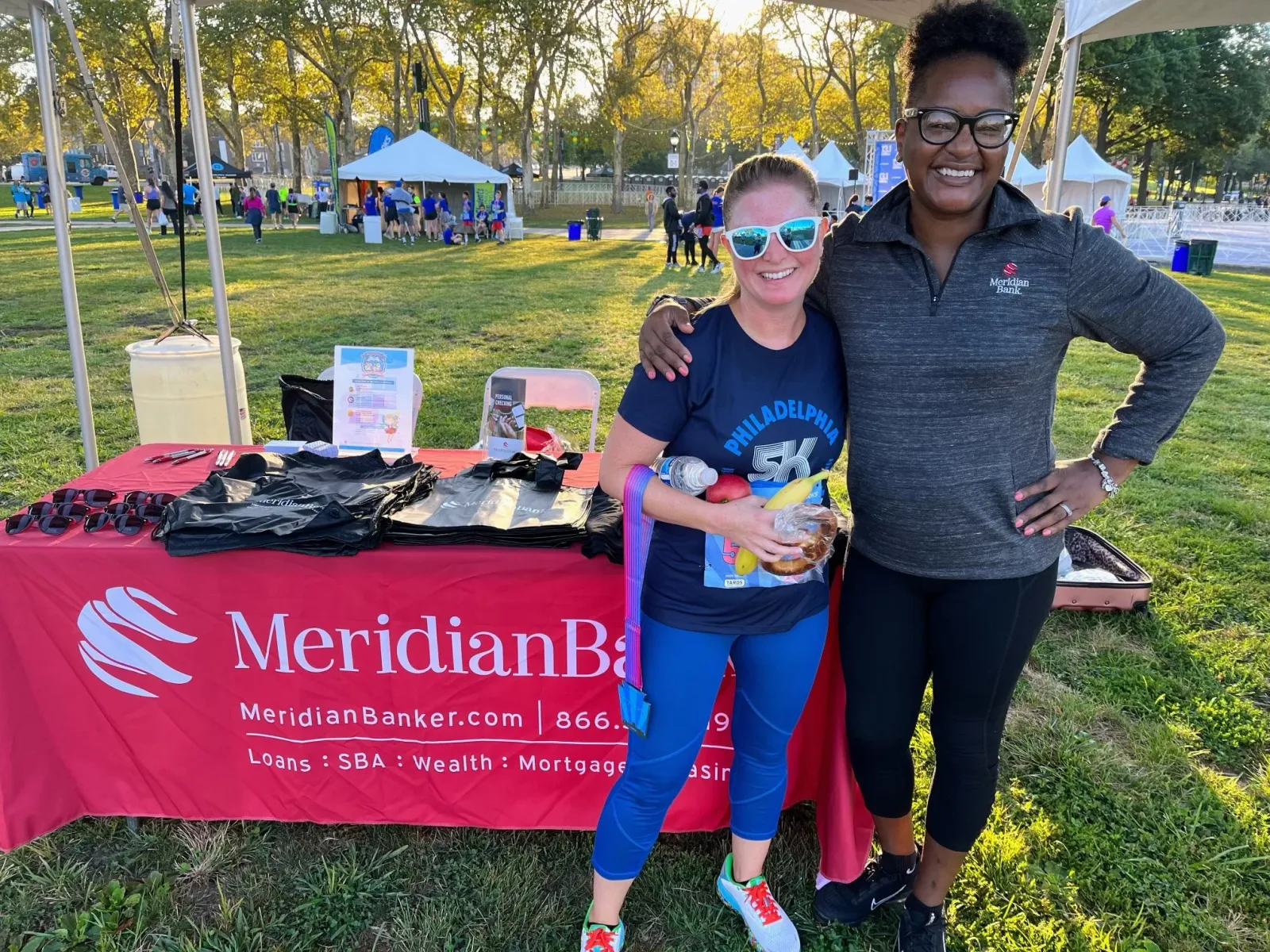 Two women smiling at a race event, one wearing a race bib and medal.