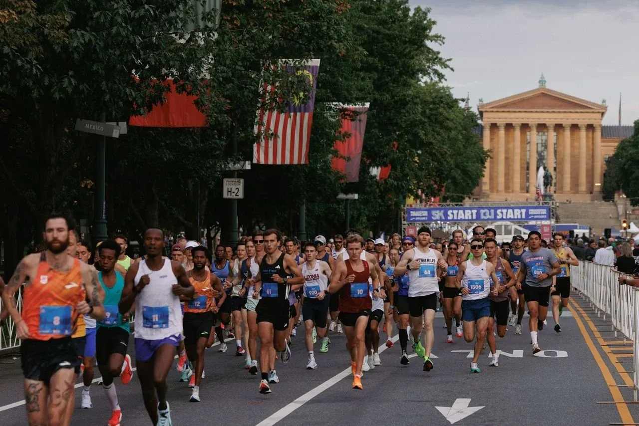 Runners starting a race in front of a large classical building, with flags and banners overhead.