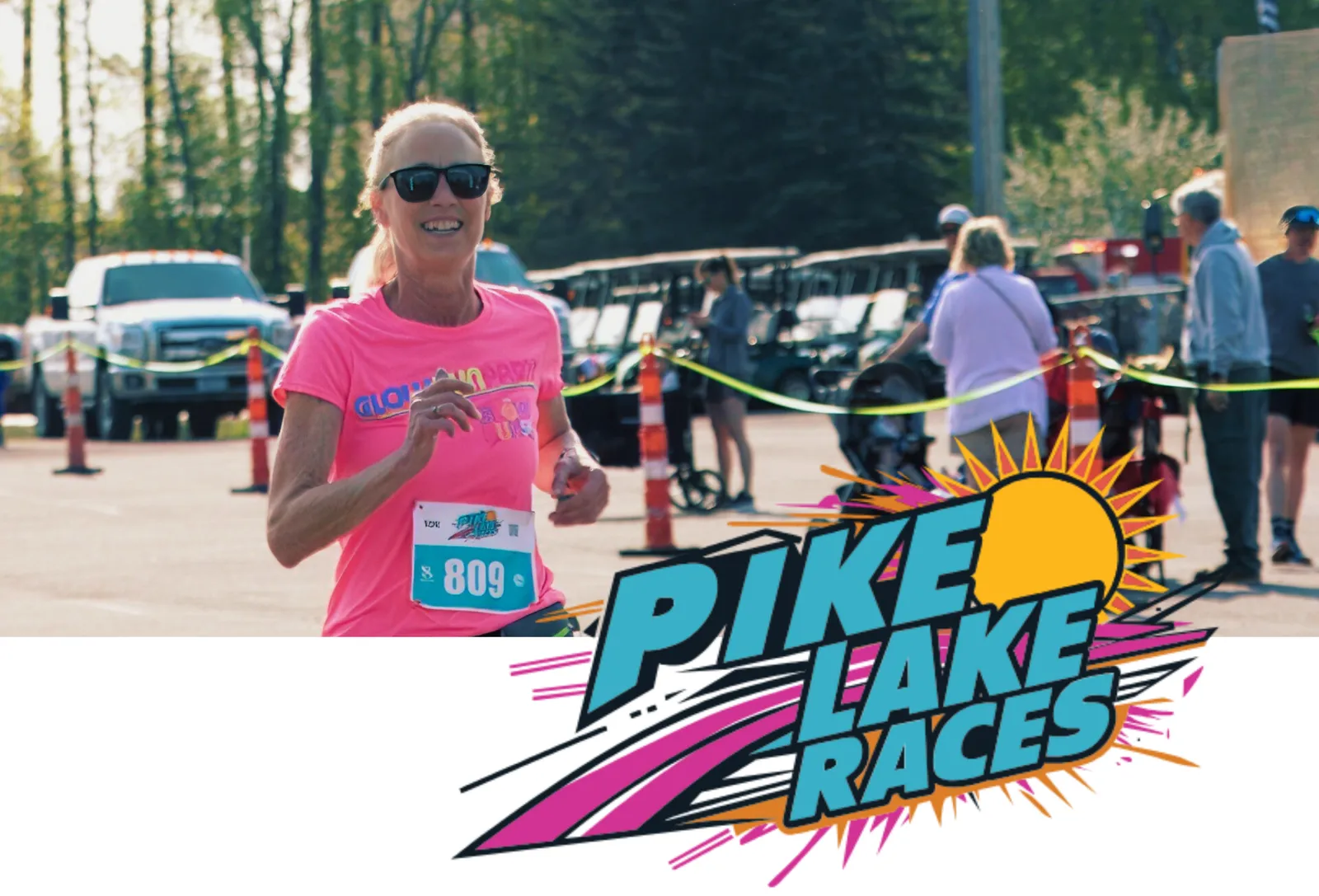 A woman smiles as she runs, wearing a bright pink t-shirt with the number 809 and a race logo. The Pike Lake Races logo is prominently displayed on the right side of the image.
