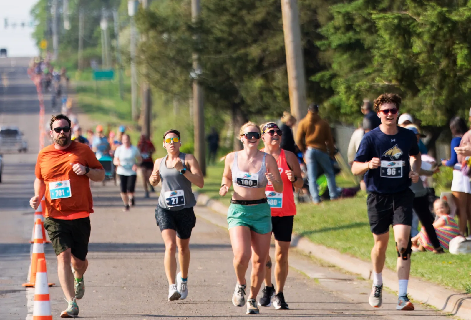 Runners on a road course, with several participants in the foreground smiling and running.