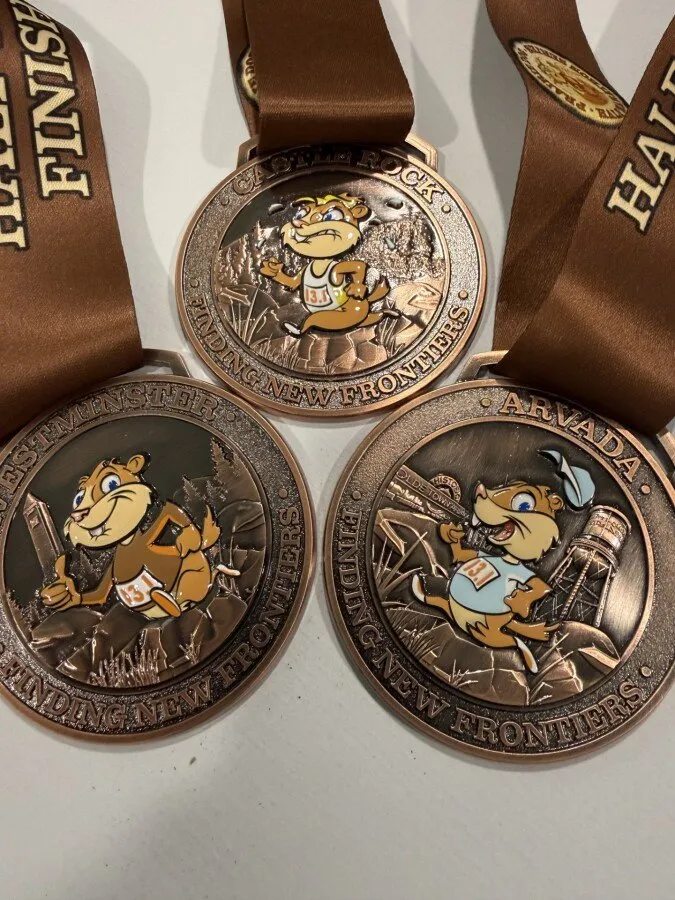 Three race medals with prairie dog mascots, each featuring different race locations and the text 'Finding New Frontiers'.