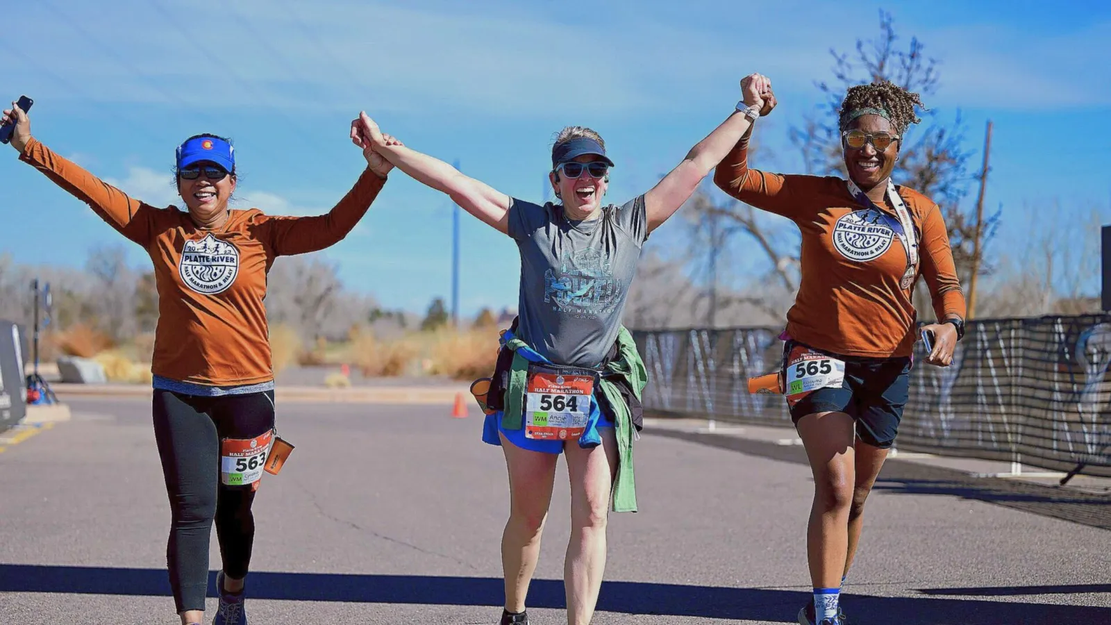 Three runners celebrating as they cross the finish line, holding hands in the air.