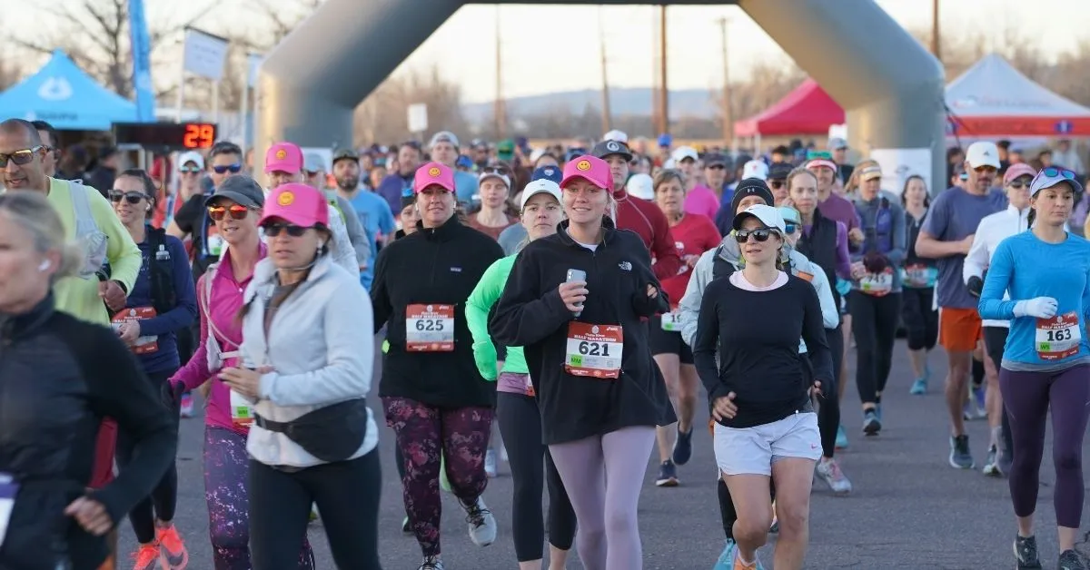 A large group of runners are starting a race, with an inflatable archway in the background.