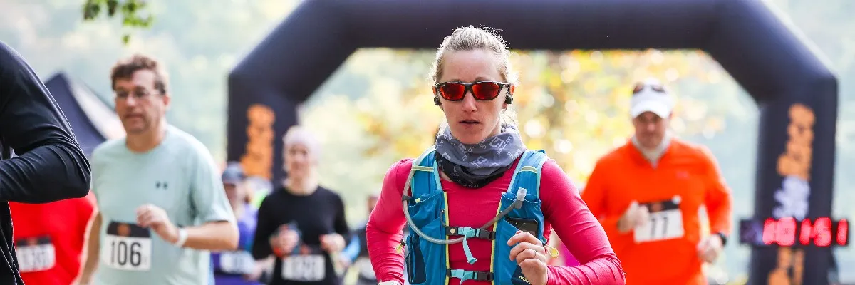 Runners crossing an inflatable archway at the start of a race, with a female runner in the foreground.