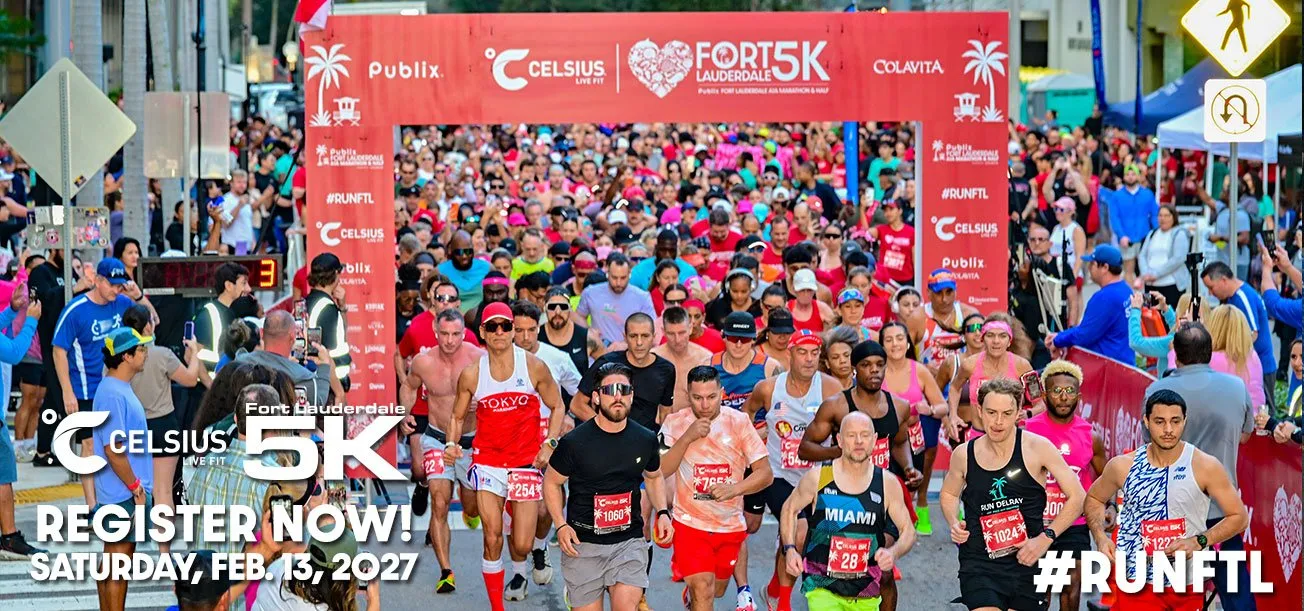 A large crowd of runners surges forward at the start line of the Fort Lauderdale 5K, with banners and palm trees visible in the background.