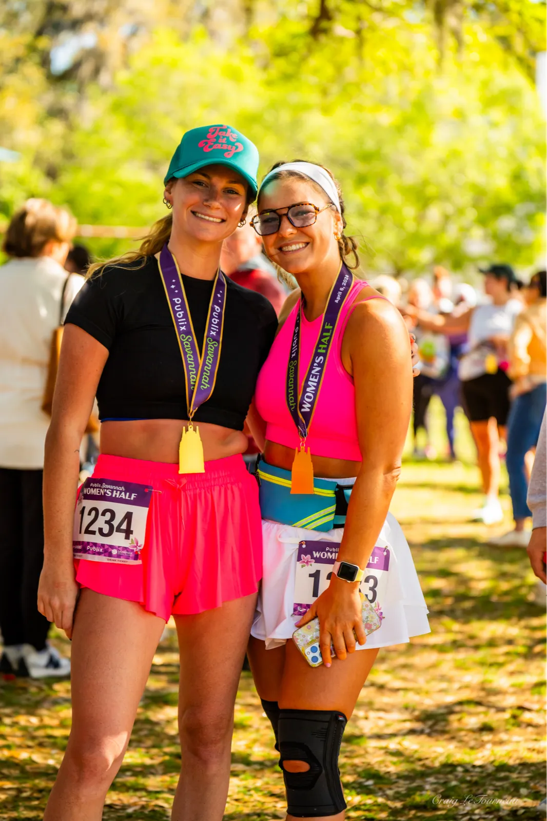Two smiling women wearing race medals and bibs, celebrating after completing a half marathon.