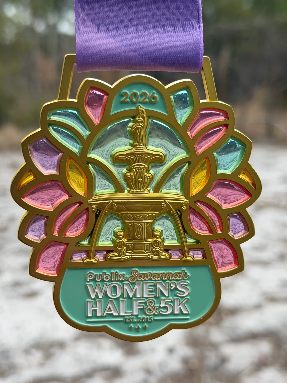 A colorful medal for the Publix Savannah Women's Half & 5K, featuring a fountain design and stained-glass-like accents.