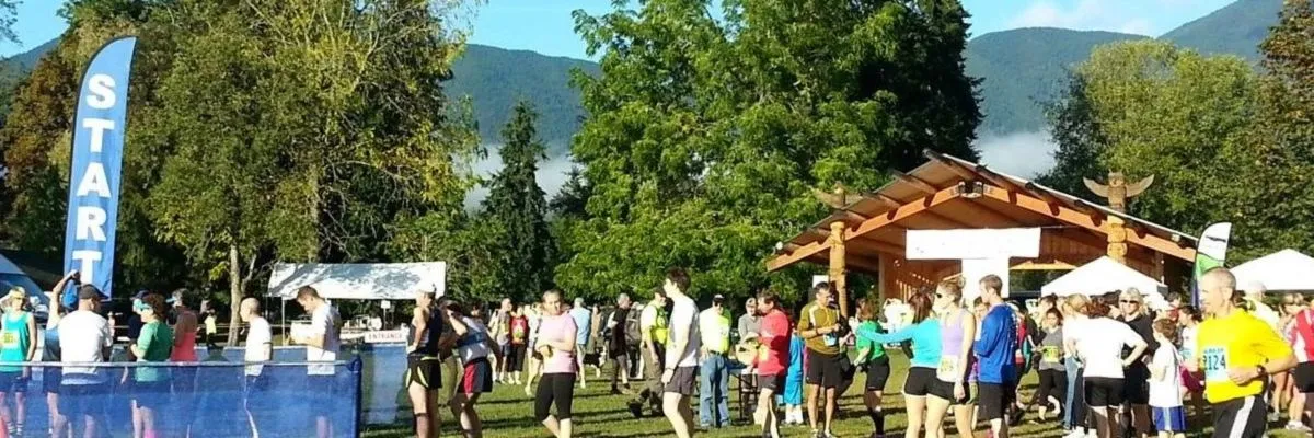 Runners gather at the start line of a race, with a blue 'START' banner and a scenic mountain backdrop.