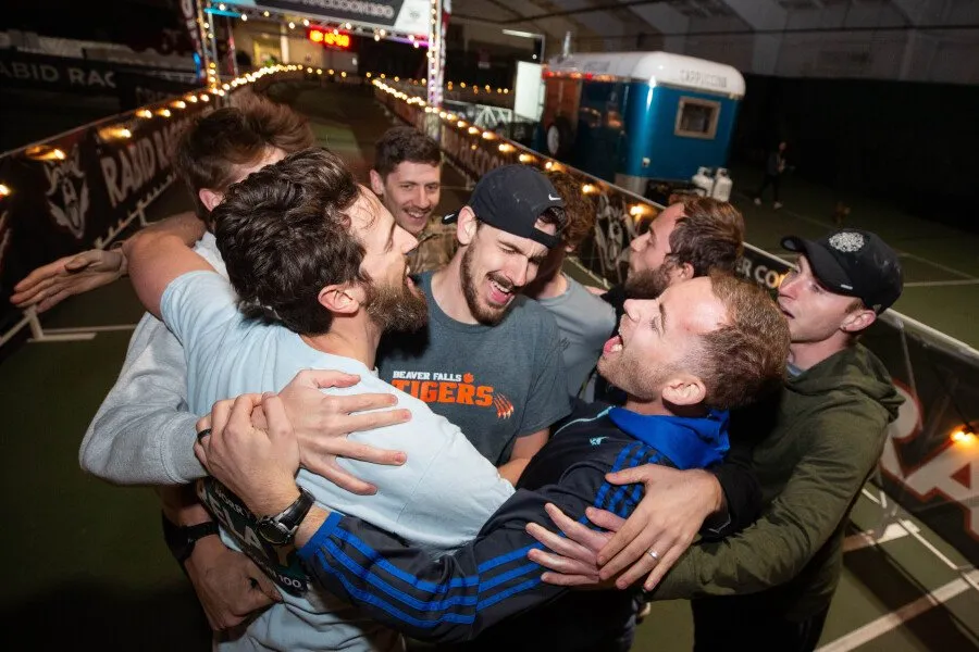A group of runners in a joyful embrace, celebrating at a race event.