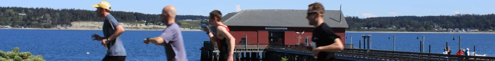 Runners on a path overlooking the water with a red building in the background.