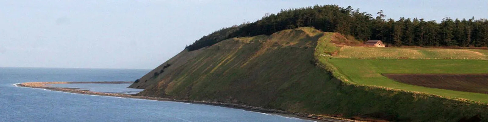 Scenic view of a coastal path with rolling green hills and the ocean.