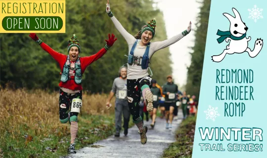 Two runners in festive holiday attire with arms raised in celebration, running on a trail during the Redmond Reindeer Romp Winter Trail Series.
