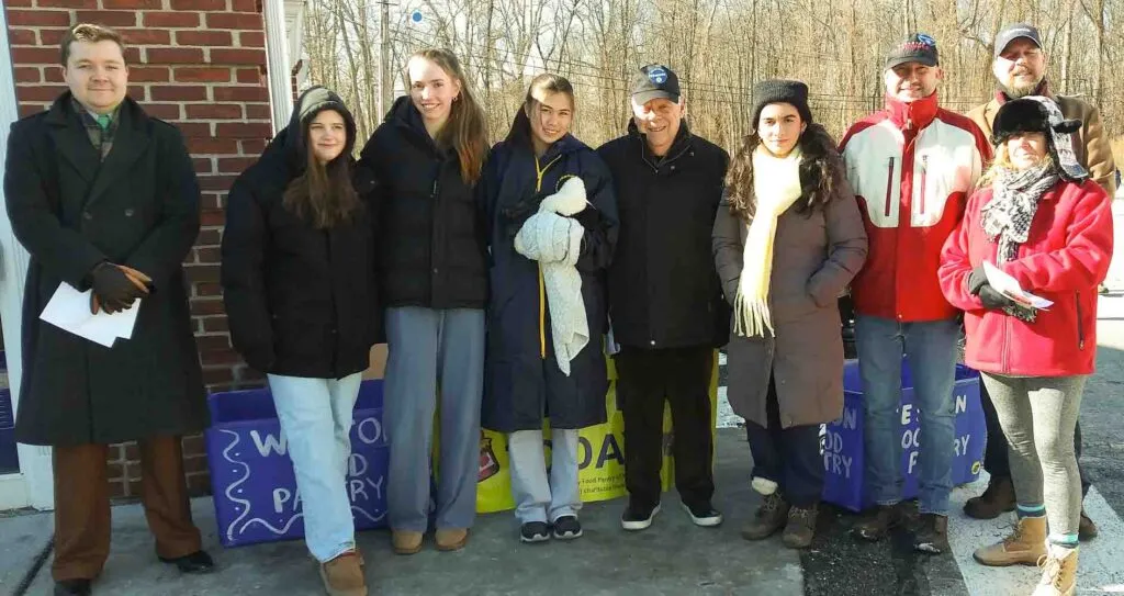 A group of people, including adults and teenagers, stand together outdoors in winter clothing, posing for a photograph.