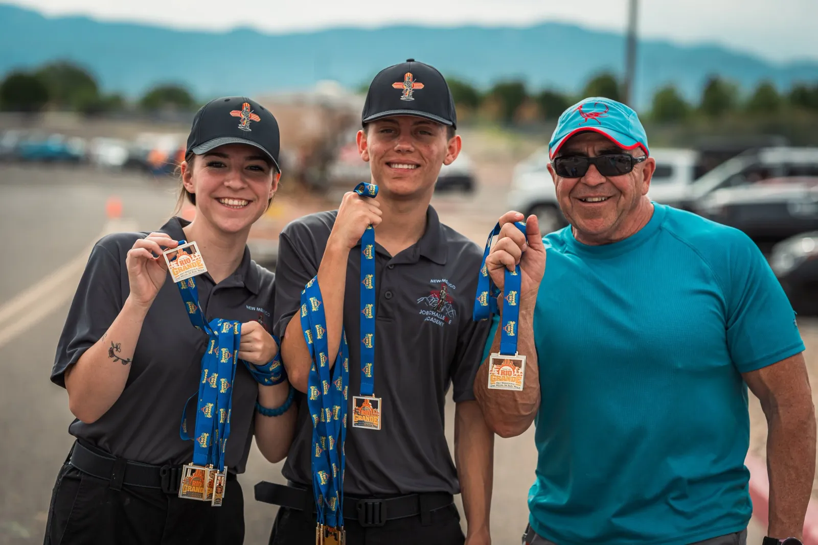 Three smiling people, two young adults and one older man, proudly display their Rio Grande Half Marathon medals.