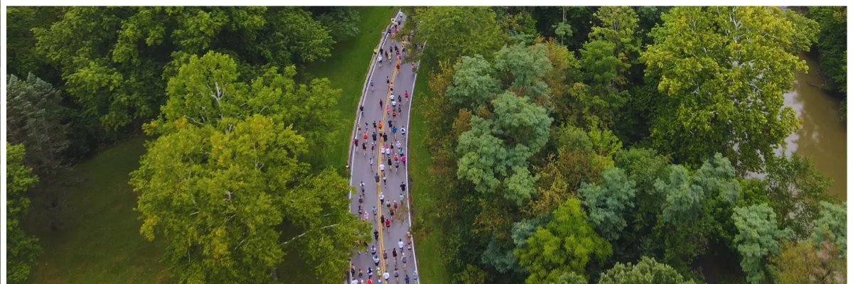 Aerial view of runners participating in the River Run Half Marathon on a tree-lined road next to a river.