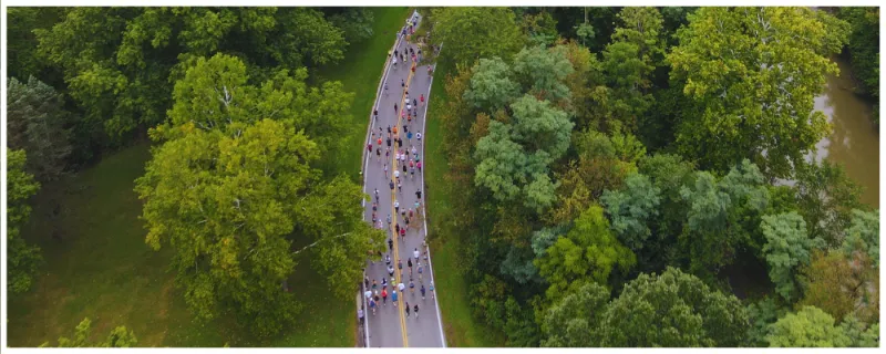 Aerial view of runners on a road through a forest next to a river during the River Run Half Marathon.