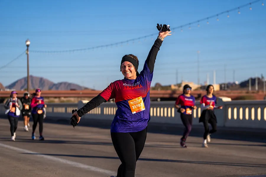 A female runner with her arm raised in celebration, smiling at the camera during the Rock 'n' Roll Arizona Marathon.