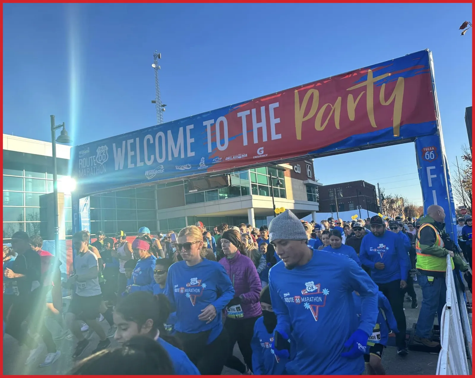 Runners gather at the start line under a large banner that reads "Welcome to the Party" for the Route 66 Marathon.