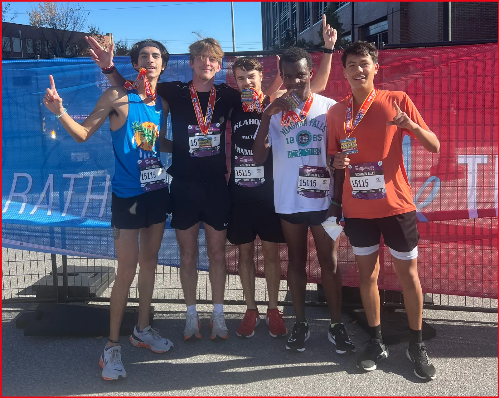 Five young men posing for a photo, all wearing race medals and bibs, with smiles and celebratory gestures.