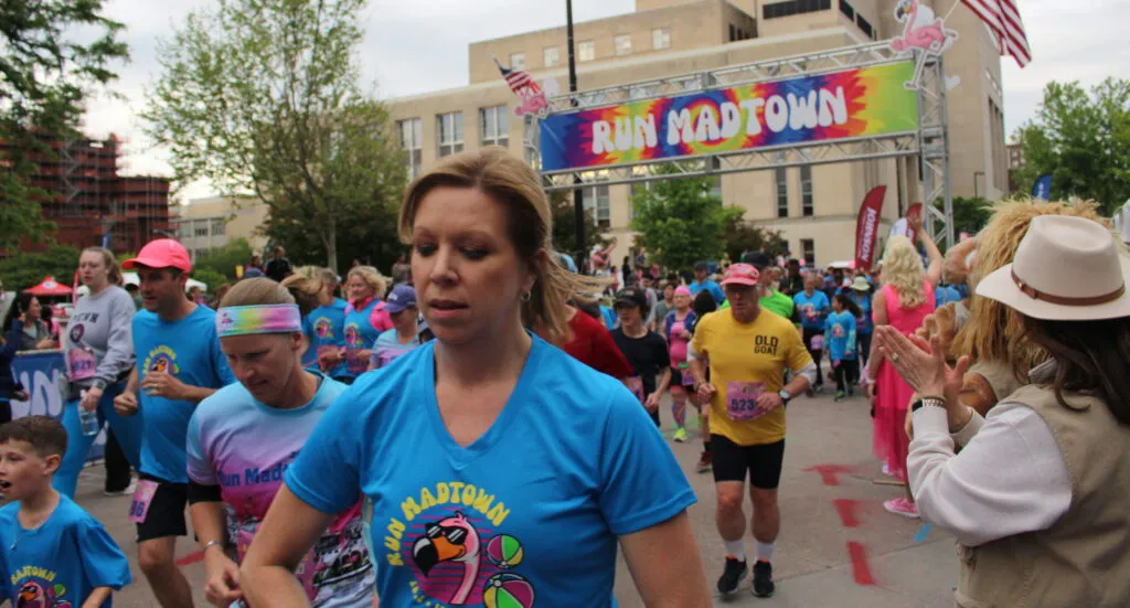 Runners starting the Run Madtown race, with a colorful banner overhead.