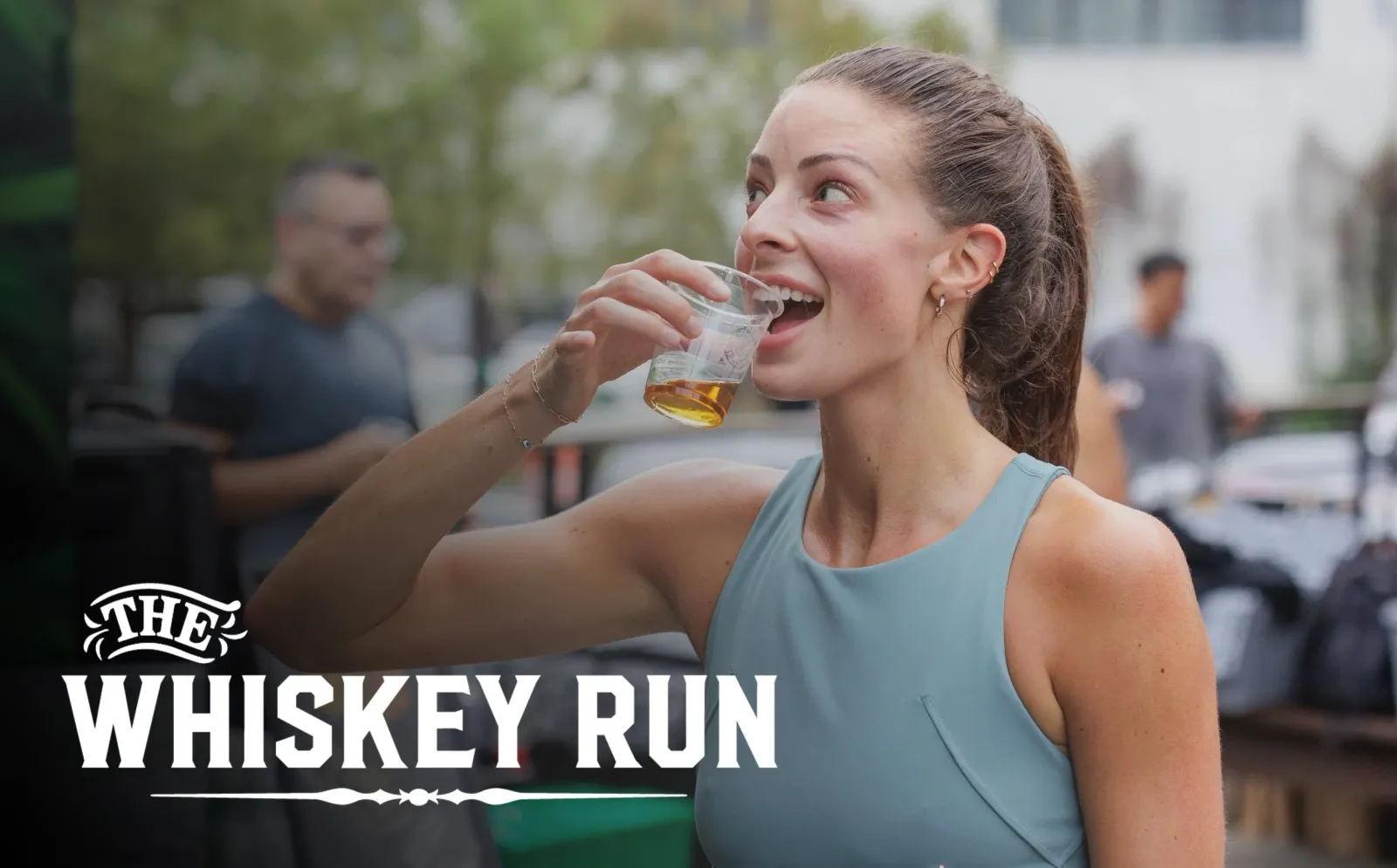 A woman in athletic wear smiles as she drinks from a small cup, with the words "THE WHISKEY RUN" overlaid on the image.