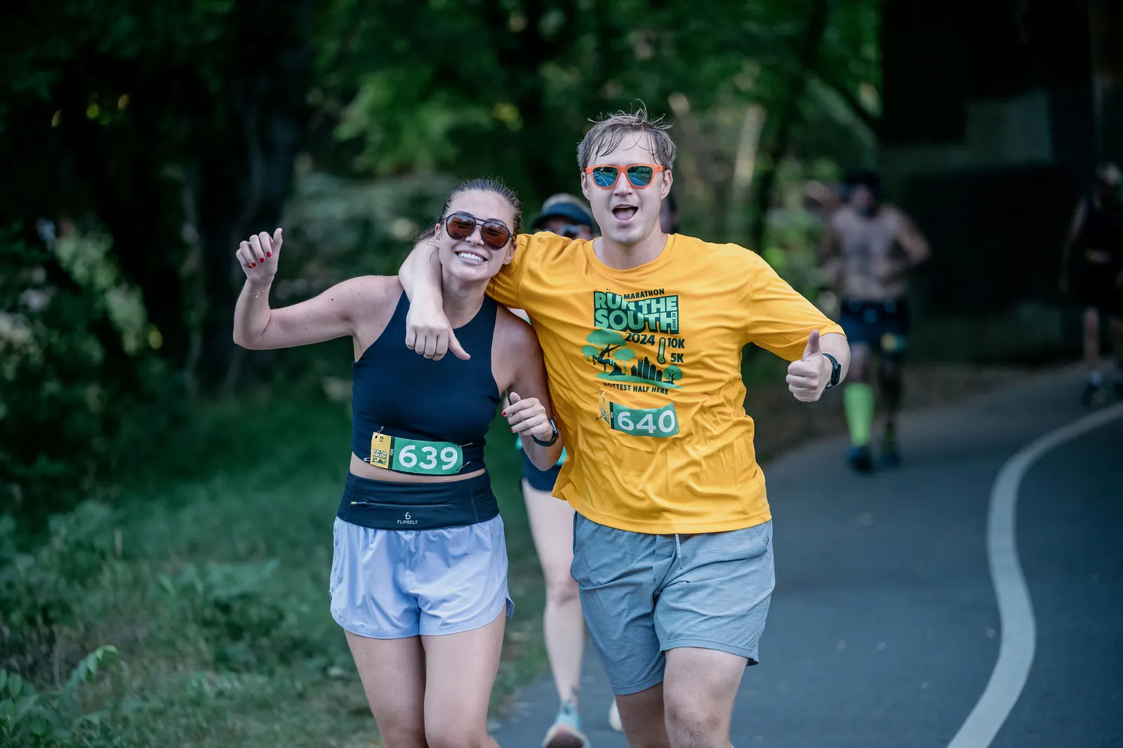 A male and female runner smile and pose for the camera during the Run The South race, with the male runner giving a thumbs up.