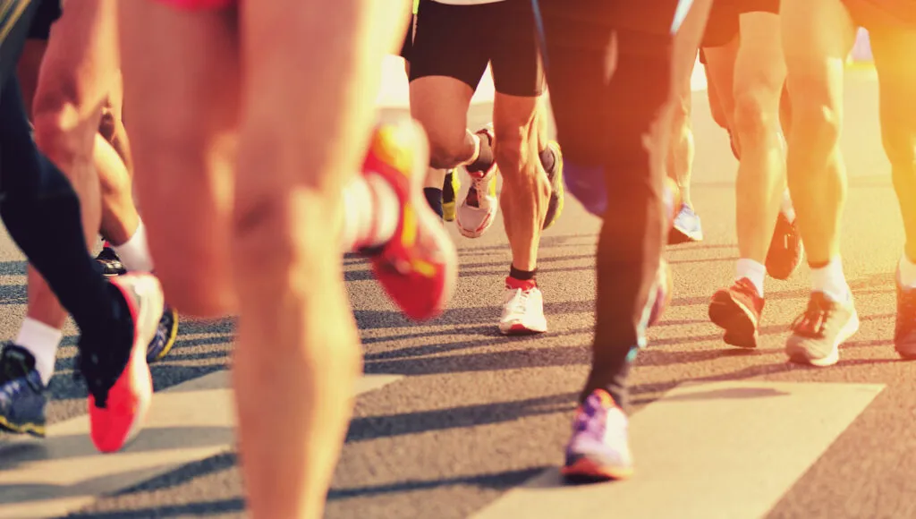 Close-up of runners' legs and feet as they start a race on a road.