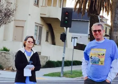 Two people standing at a crosswalk, one wearing a race t-shirt.