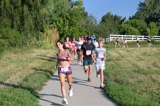 A group of runners, including a woman in the foreground and a young boy, running on a paved path with grassy areas on either side.