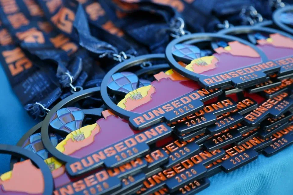 A close-up, slightly angled view of a stack of Run Sedona 2026 race medals, featuring a hot air balloon and desert landscape design.