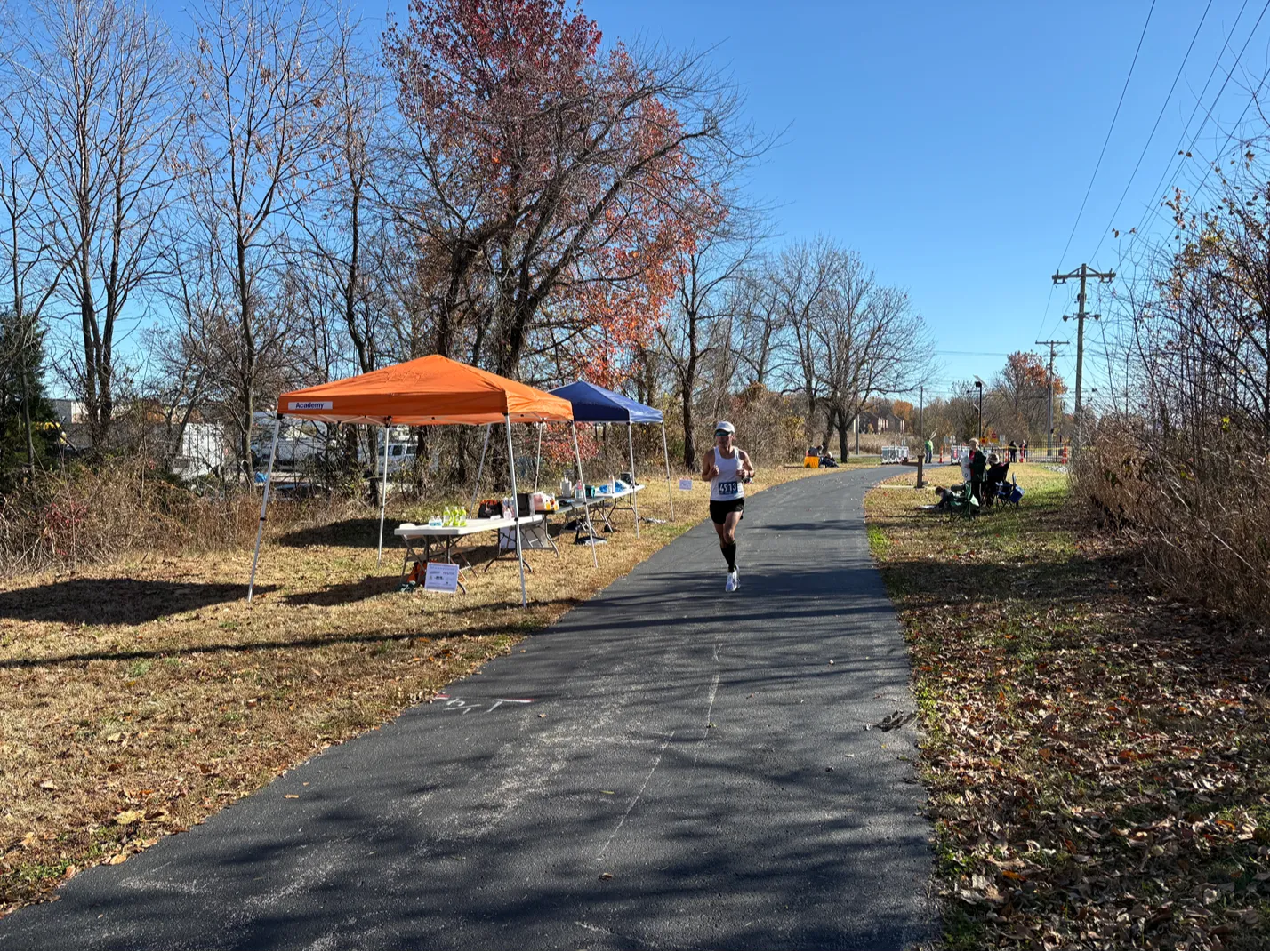 A runner on a paved path with trees and aid stations in the background.