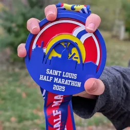 A hand holds up the Saint Louis Half Marathon 2025 medal.