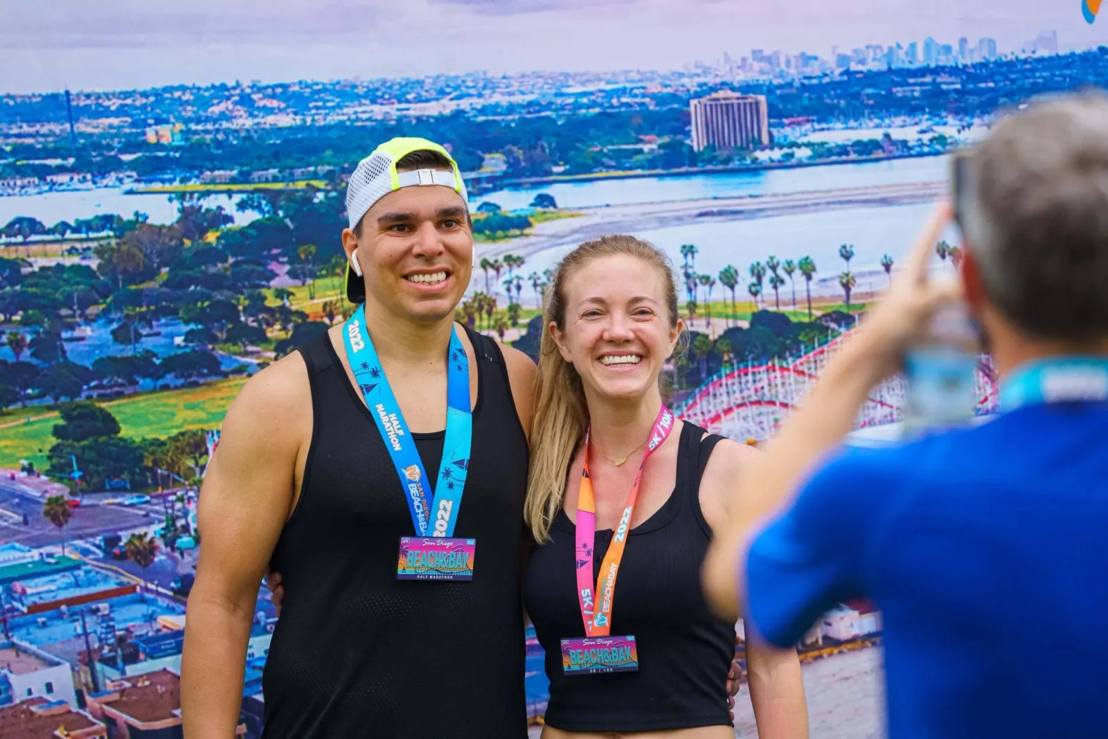 A smiling couple poses for a photo, both wearing race medals from the San Diego Beach & Bay Half Marathon.