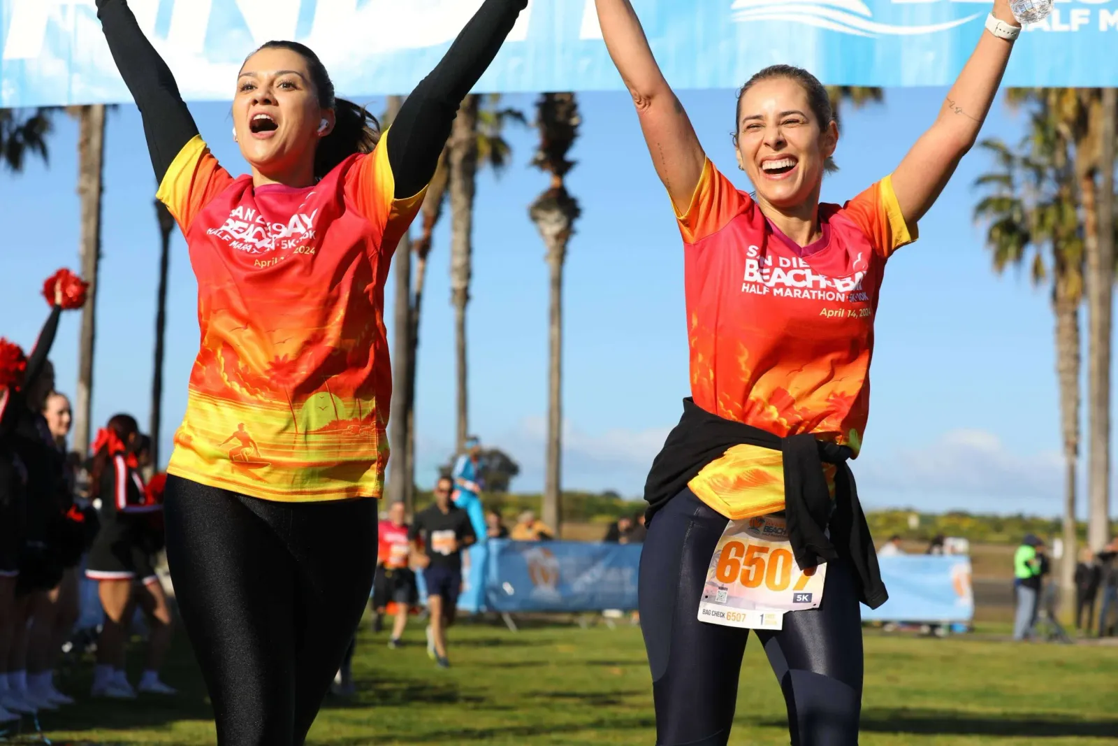 Two women with their arms raised in celebration at the finish line of the San Diego Beach Bay Half Marathon.
