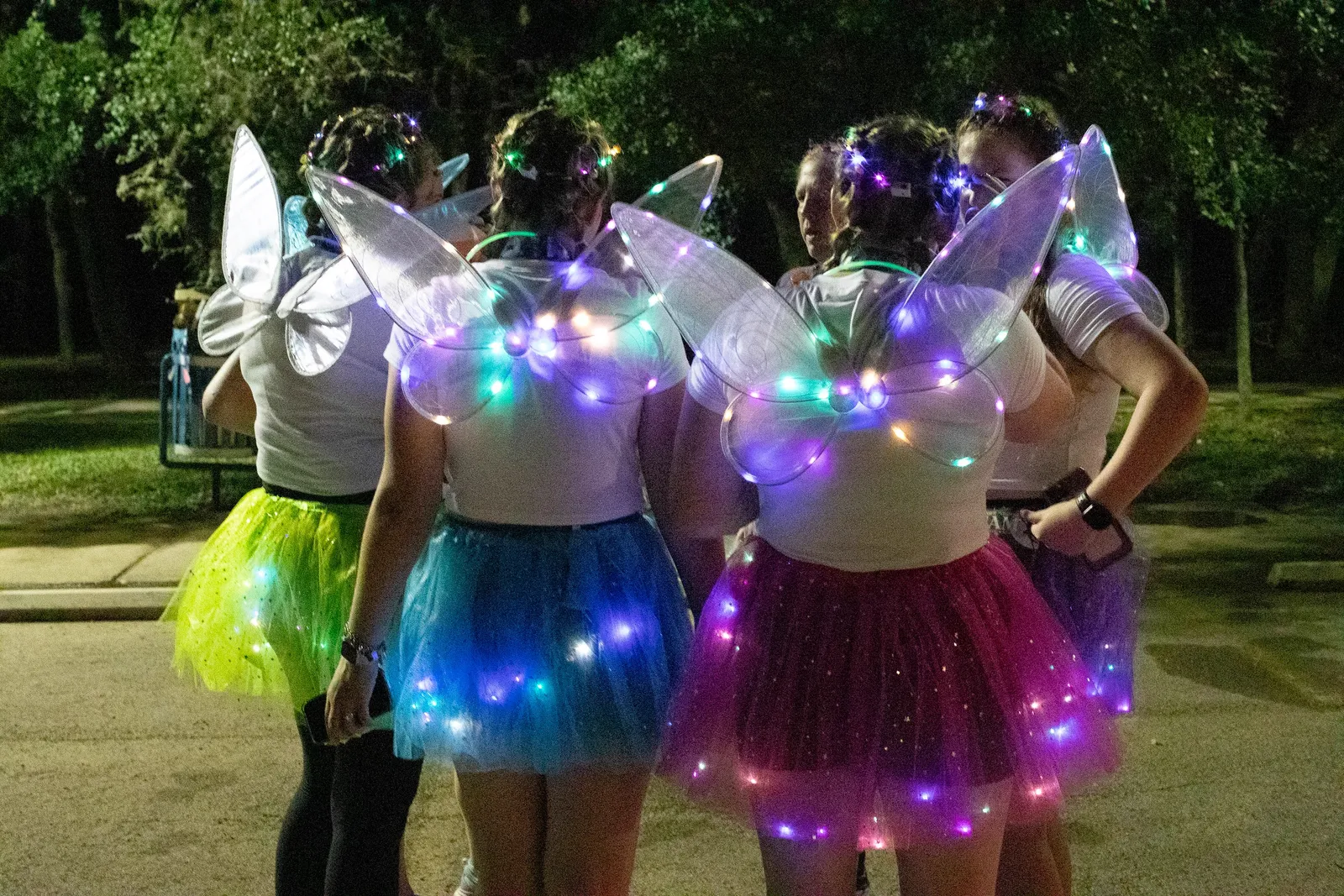 Group of people in fairy costumes with illuminated wings and tutus at night.