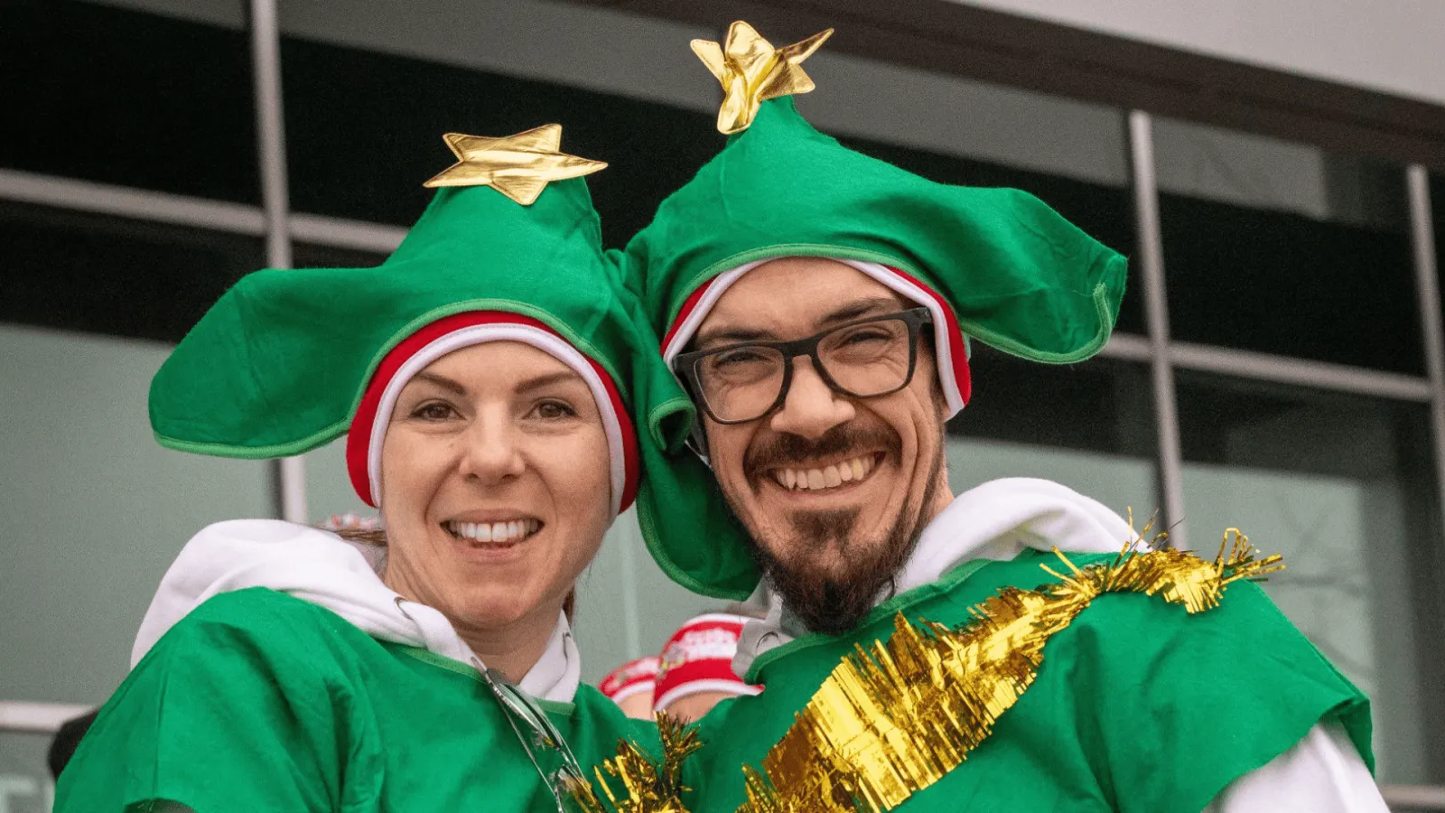 Two people dressed as elves with green hats and gold trim, smiling at the camera.