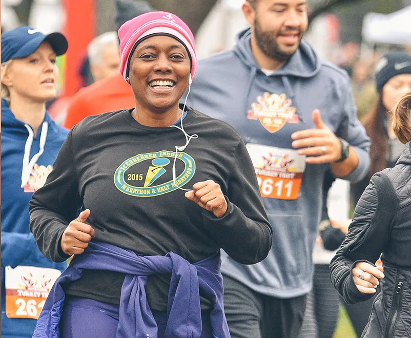 A woman smiles as she runs in a race, with other runners behind her.