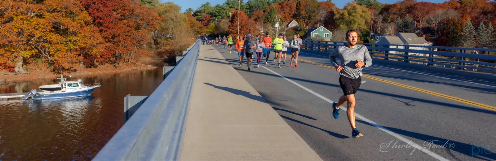 Runners on a bridge with fall foliage and a river below.